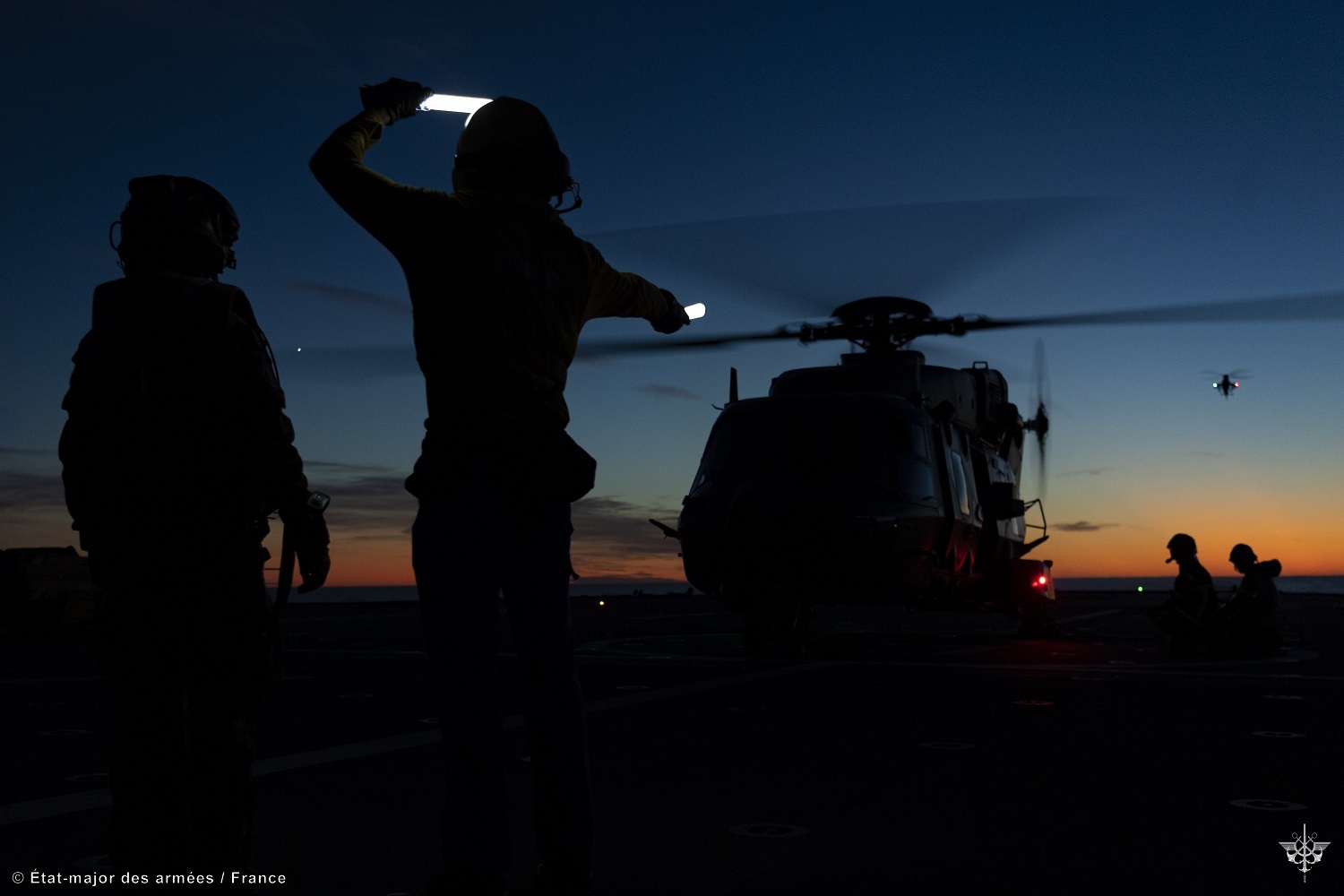 Un hélicoptère décolle de nuit du pont d'un porte-hélicoptères