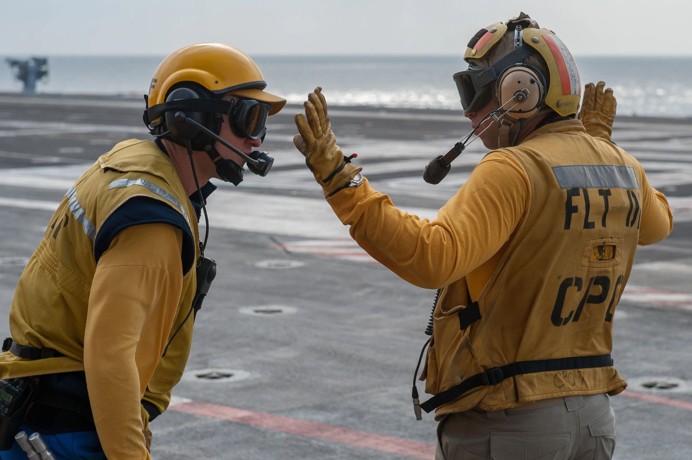 Deux directeurs de pont d'envol (français à gauche, américain à droite) attendent l'appontage d'un MH3C-2A Greyhound sur le porte-avions Charles de Gaulle